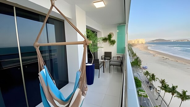 Un balcón con una hamaca, sillas y vista al mar.