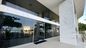 Un edificio moderno con amplios ventanales de vidrio, un pilar de mármol y el reflejo de árboles y un edificio en el cristal.