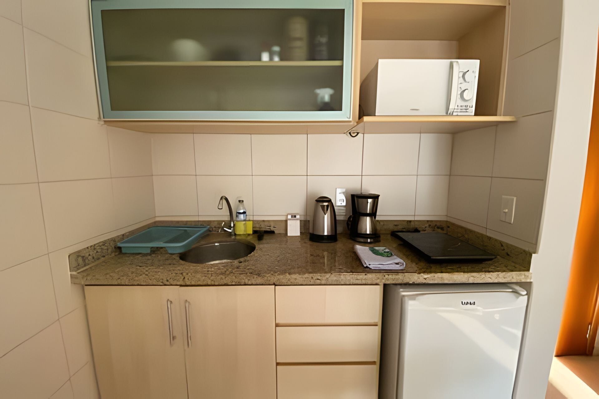 Una cocina compacta con un lavamanos, una cafetera, un hervidor y un refrigerador.