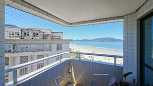 Ein Balkon mit Blick auf Strand und Gebäude. Zwei Stühle und ein Blumentopf sind zu sehen.
