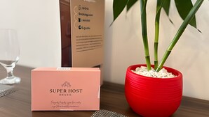 A Super Host branded box, a red pot with bamboo, and a glass of water on a wooden table.