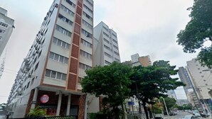 A multi-story building with a prominent vertical feature, a tree-lined street, and parked cars.