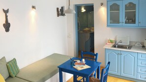 En kompakt opholdsstue med et blåt spisebord, en bænk og et tekøkken med blå skabe.