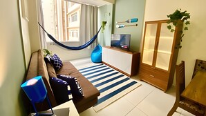A living room with a hammock, a TV, a cabinet, and a plant. - SHB - Beachfront in Pitangueira, Guaruja (Guarujá)