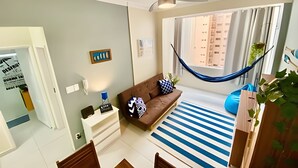 A living room with a brown sofa, a white side table, a blue hammock, and a striped rug. - SHB - Beachfront in Pitangueira, Guaruja (Guarujá)