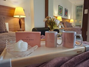 Une chambre d’hôtel avec un lit, une table de chevet avec une lampe, un vase avec des fleurs et deux tasses sur la table.