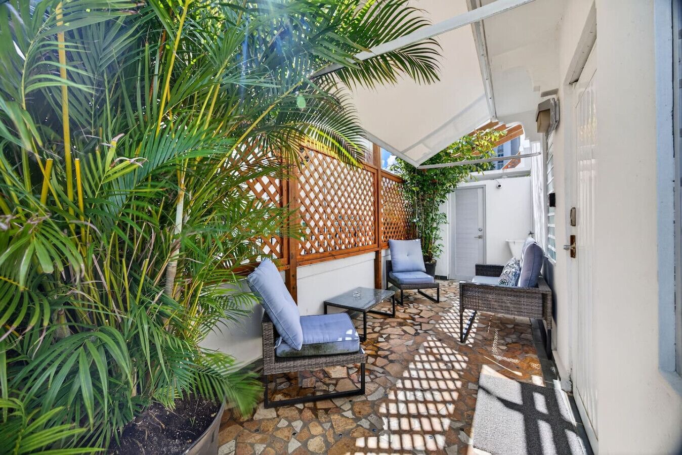 A patio with a stone floor, two blue cushioned chairs, a wicker sofa, and a wooden lattice partition.