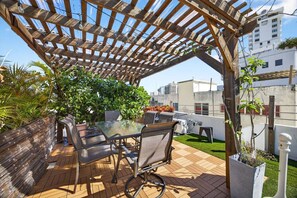 Une terrasse extérieure dotée d’une pergola en bois, d’une table en verre et de chaises.