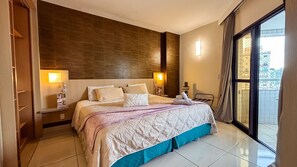 Une chambre d’hôtel avec un grand lit, deux tables de chevet, une commode, une fenêtre avec des rideaux et une vue sur les bâtiments environnants.