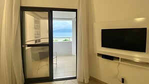 A room with a sliding glass door leading to a balcony with a view of the sea. A flat-screen TV is mounted on the wall. - SHB - Ocean view flat in Boqueirão! Wi-Fi / Pool (Santos)