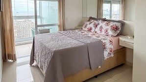 Ein modernes Schlafzimmer mit einem großen Bett, einem Nachttisch, einem Spiegel und Blick auf die Stadt durch große Fenster.
