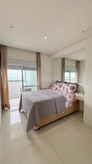 Quarto moderno com uma cama grande, mesa de cabeceira, espelho e vista da cidade através de amplas janelas.