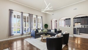 A spacious living room with a dark sofa set, a round coffee table, and a modern chandelier. - 6BD Luxury Retreat w Backyard & Access Golf Course (Frisco)