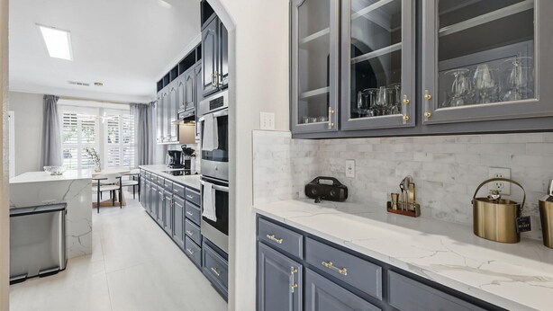 A modern kitchen with grey cabinetry, a marble countertop, and a built-in oven. - 6BD Luxury Retreat w Backyard & Access Golf Course (Frisco)