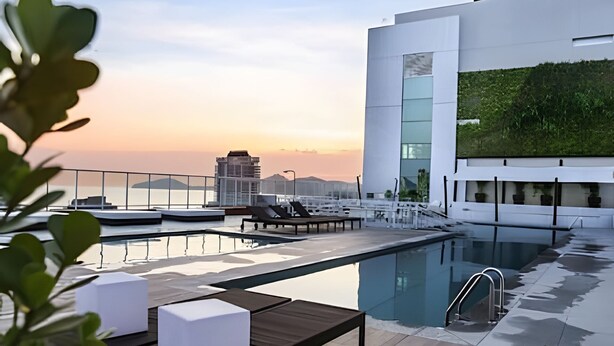 A rooftop pool area with lounge chairs and a glass balustrade, overlooking a cityscape at sunset. - SHB - High Standard with Panoramic View! (Santos)
