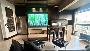 A modern kitchen with a large TV, a dining area with stools, and a living room with black leather furniture. - SHB - High Standard with Panoramic View! (Santos)