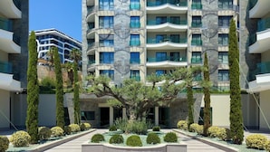 A modern building with multiple balconies, a central courtyard with trees, and a clear sky. - Apartment 1+1 Qoople Excellence С49 With a terrace on the 1st line of the sea (Alanya)