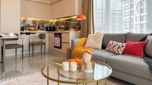 A modern living room with a sofa, coffee table, and a kitchen in the background. - Apartment 1+1 Qoople Excellence С49 With a terrace on the 1st line of the sea (Alanya)