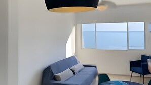 Un salón moderno con sofá, mesa de comedor y un ventanal con vistas al mar.