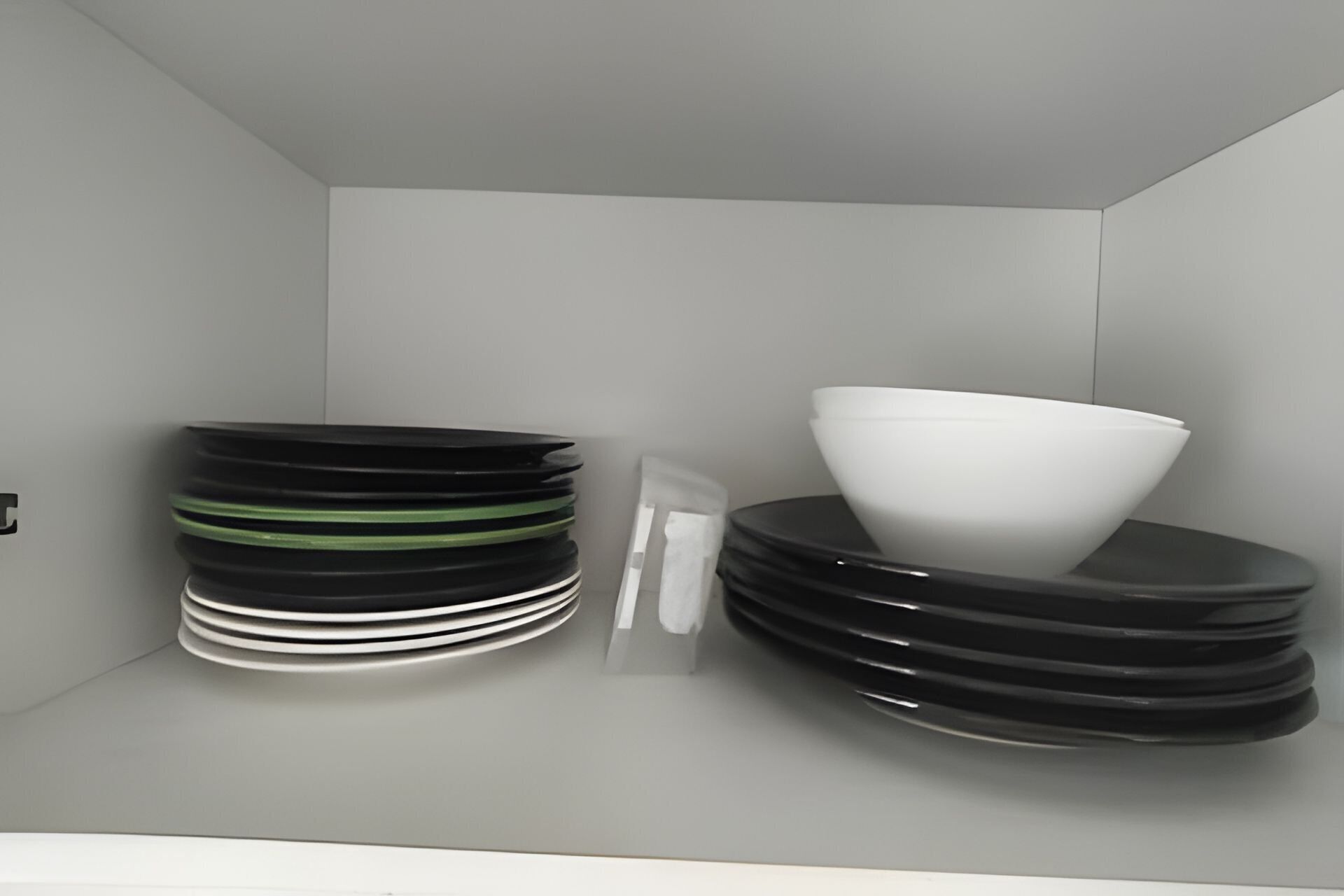 Un espace de rangement où sont empilées des assiettes et où se trouve un bol blanc.