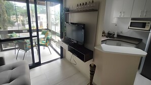 Een moderne woonkamer met een flatscreen-tv, een eethoek met een glazen tafel, en een keuken met witte kasten en een magnetron.