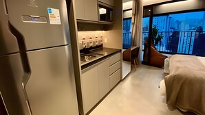 Een moderne hotelkamer met een kitchenette, een bed, een groot raam met uitzicht op de stad, en een balkon.