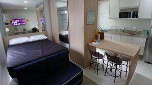 A modern hotel room with a bed, a desk, and a kitchenette. - SHB - Wake Up with the Breeze: Charming Apartment in Embaré (Santos)