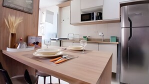 A modern kitchen with white cabinets, a stainless steel refrigerator, and a wooden island with plates and cutlery. - SHB - Wake Up with the Breeze: Charming Apartment in Embaré (Santos)