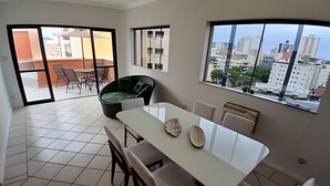 A modern dining area with a white table and chairs, a black sofa, and a view of the city through large windows. - SHB - Guarujá Private Pool and Leisure at Enseada (Guarujá)