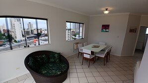 A spacious room with a large window, a dining table with chairs, a sofa, and a small kitchen area. - SHB - Guarujá Private Pool and Leisure at Enseada (Guarujá)