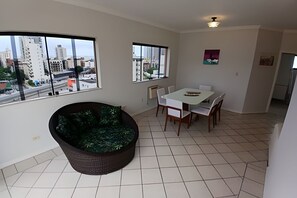 Una habitación amplia con un gran ventanal, una mesa de comedor con sillas, un sofá y una pequeña zona de cocina.