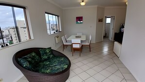 A modern living room with a large window, a dining area with a table and chairs, and a kitchen area. - SHB - Guarujá Private Pool and Leisure at Enseada (Guarujá)