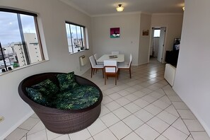 Una sala de estar moderna con un ventanal grande, un comedor con mesa y sillas, y una zona de cocina.