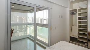A bedroom with a sliding glass door leading to a balcony, a bed with a patterned mattress, and a built-in shelving unit with a mattress on top. - SHB - Style and Comfort with Gourmet Area (Guarujá)