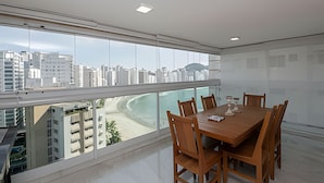 A modern dining room with a large table and chairs, large windows offering a city view, and a clean, minimalist interior design. - SHB - Style and Comfort with Gourmet Area (Guarujá)