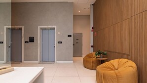 A modern lobby with two elevators, a reception desk, and two round, mustard-colored seating areas. - Studio pet Friendly a 350m do Nubank Parque (São Paulo)