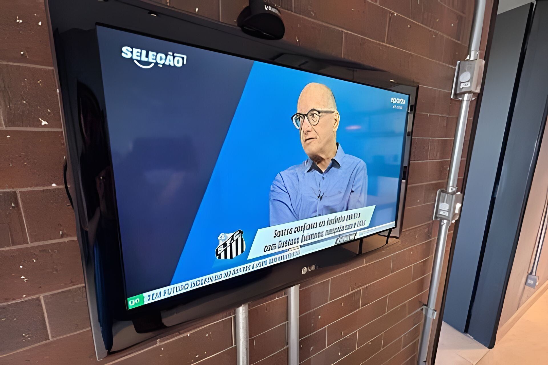 Un televisor fijado en una pared de ladrillo mostrando un noticiero.