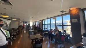 A restaurant with a view of the sea, wooden tables and chairs, and pendant lighting. - SHB - Discover the Magic of a Panoramic View (Santos)