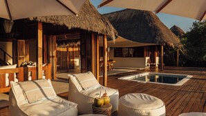 A wooden deck with lounge chairs and a pool, surrounded by thatched-roof structures. - Rio Azul Mozambique  (Bartolomeu Dias Point)