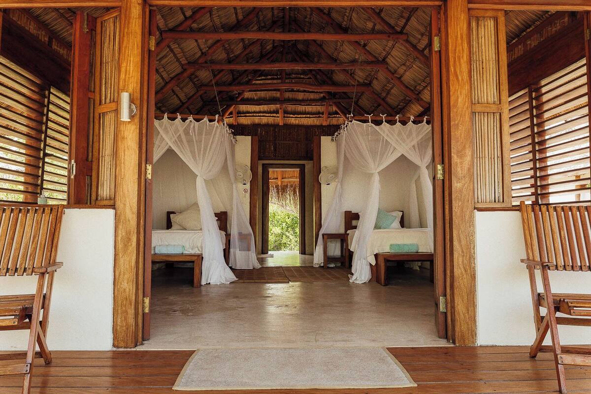 A room with two beds, each with a canopy, wooden flooring, and a thatched roof.