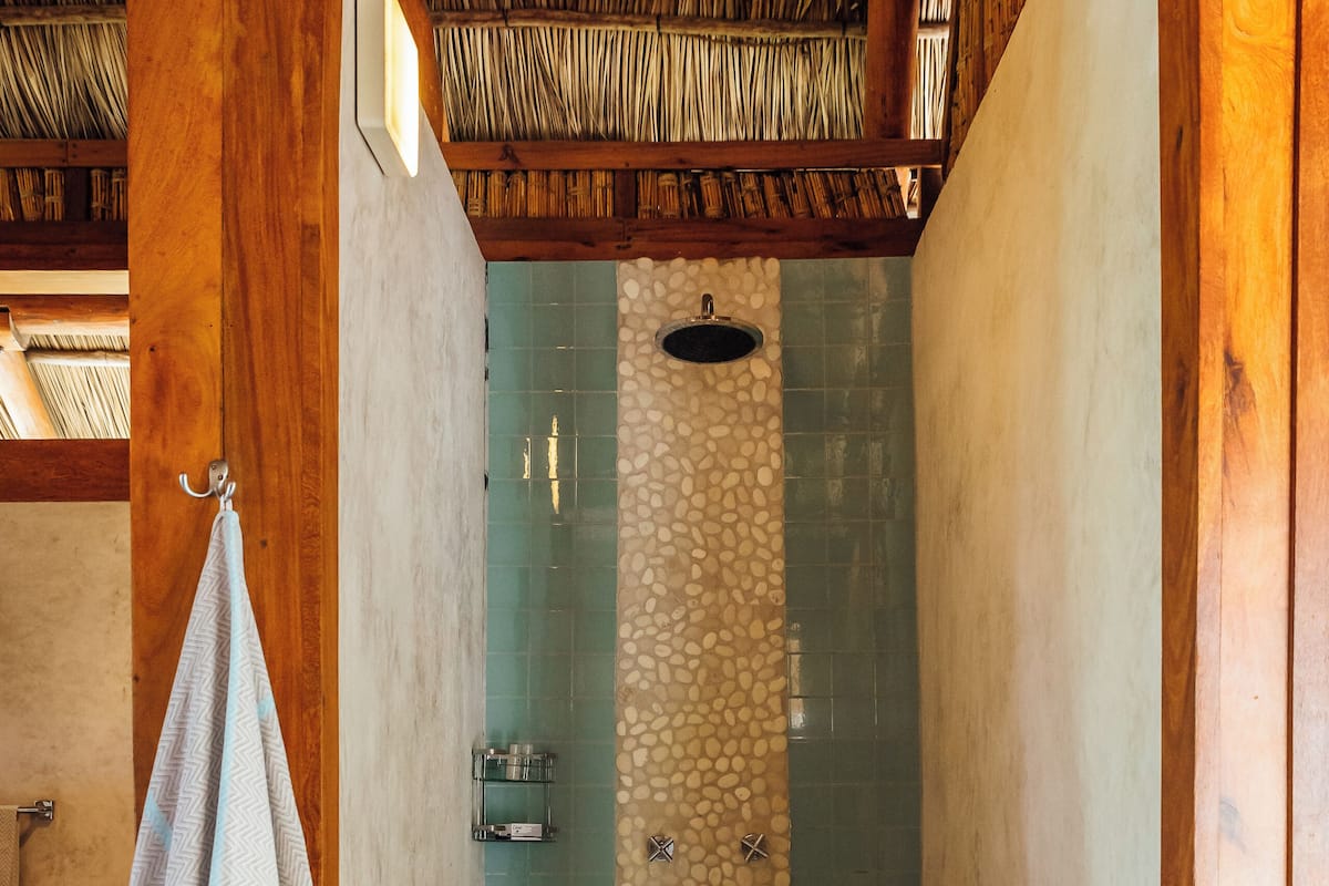 A shower area with a stone wall, wooden beams, and a hanging towel.