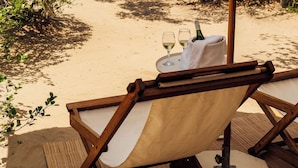 A beachside lounge with a view of the sea, a table with a bottle and glasses, and a wooden chair. - Rio Azul Mozambique  (Bartolomeu Dias Point)