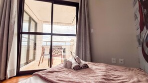 A bedroom with a large window, a bed with a pink blanket, and a chair outside. - SHB • Feet in the Sand | Balcony with Sea View (Santos)