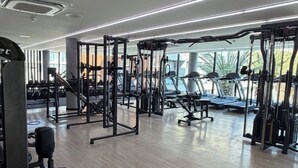 Uma academia moderna com diversos equipamentos de exercício, amplas janelas e piso de madeira limpo.
