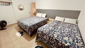 Un dormitorio con dos camas, un espejo redondo, un ventilador y una puerta que da a otra habitación.