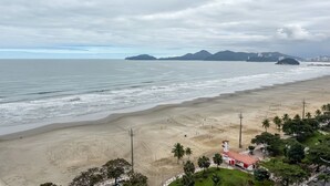 Ein Strand mit einem roten Gebäude, Palmen und Bergen im Hintergrund.