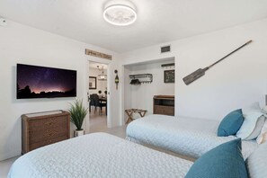 A bedroom with two beds, a night sky painting, a ceiling fan, and a dining area visible through an open door. - H-346 -Third Floor - Sunset Views From The Lanai! (Naples)