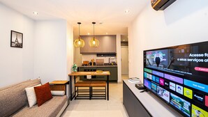 A modern living room with a sofa, a dining table, and a TV displaying various channels. - SHB • Praiamar Shopping | Beach Just Steps Away (Santos)