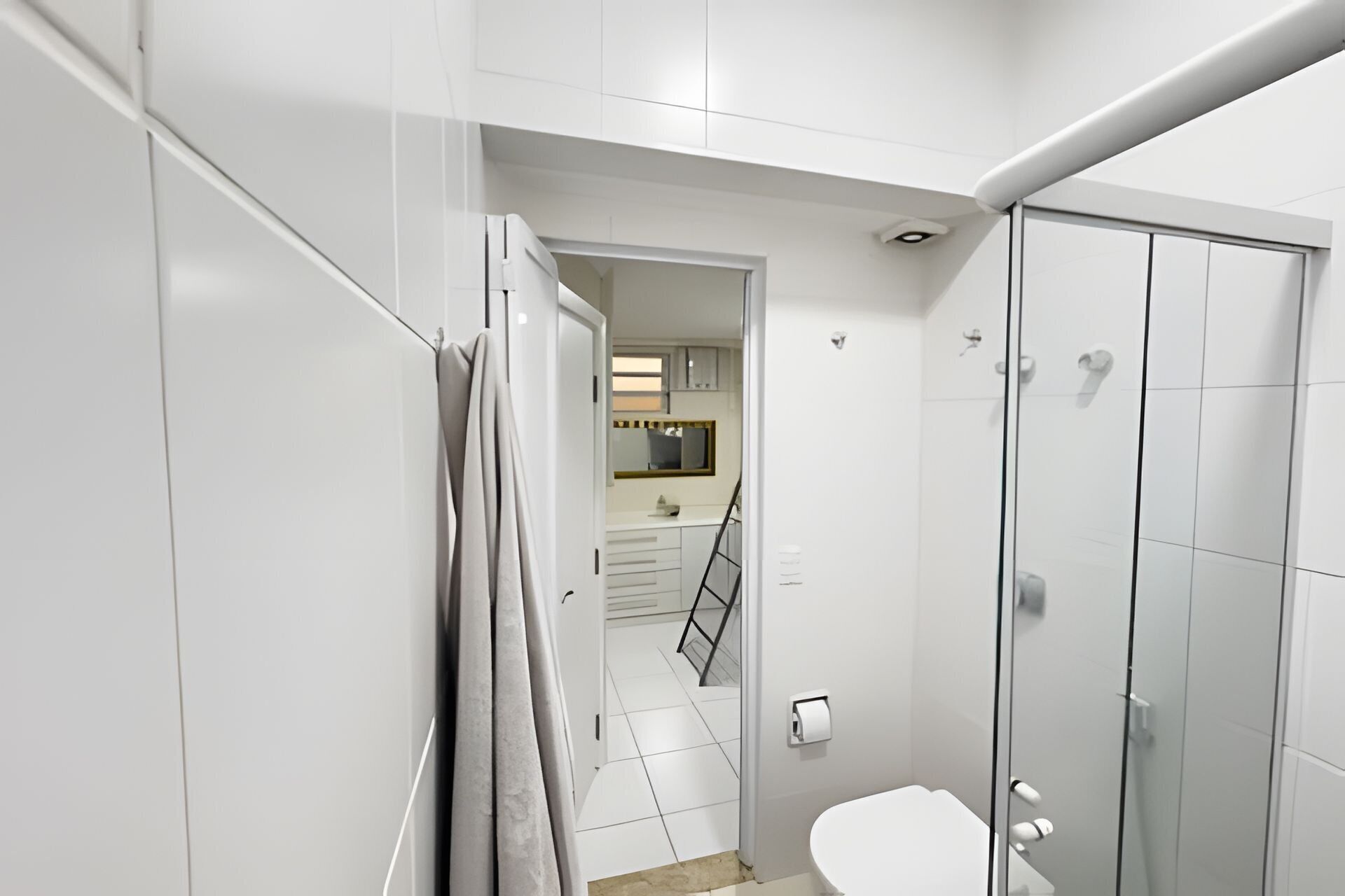 A modern bathroom with a glass shower enclosure, a toilet, and a sink area visible through an open door.