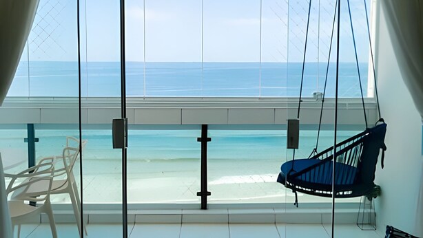 A balcony with a view of the ocean, a hanging chair, and a white chair. - SHB - Wake Up to the Blue of the Sea at Your Window! (Guarujá)